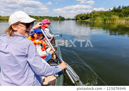 Woman two children enjoy having fun paddling canoe rent across lake river water wearing bright orange life vests hot sunny summer day. Healthy recreational activity lifestyle vacation trip journey 123876946