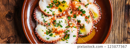 Tender octopus slices on a rustic plate, drizzled with olive oil, sprinkled with paprika, and garnished with fresh parsley, creating a flavorful, traditional Spanish dish, banner 123877367
