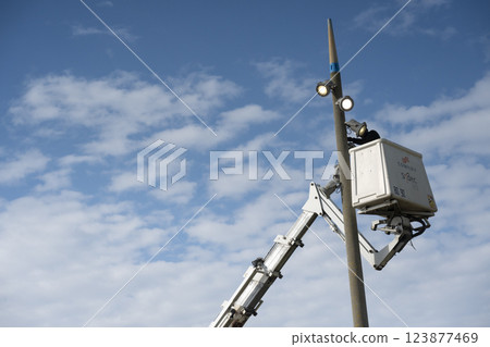 Worker conducts maintenance on a tall light pole using a lift beneath a clear blue sky with Worker conducts maintenance on a tall light pole using a lift beneath a clear blue sky with 123877469