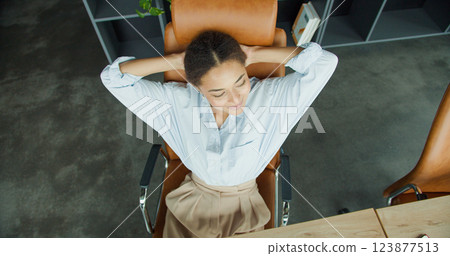 Relaxed young woman leaning back in a leather chair in a modern office, smiling with hands behind her head and enjoying a break during work 123877513