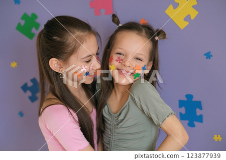 Happy kids who have decorated their faces and backgrounds with pieces of multicolored jigsaw puzzles. Concept for Disability Pride Month, world brain day, mental and neurological health Happy kids who have decorated their faces and backgrounds with pieces of multicolored jigsaw puzzles. Concept for Disability Pride Month, world brain day, mental and neurological health 123877939