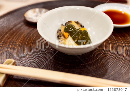 Refined serving of abalone sashimi with sea urchin presented in an elegant ceramic dish 123878047