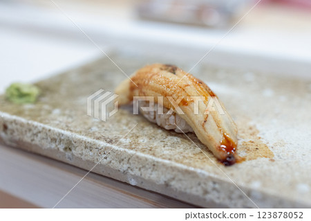 Conger eel nigiri sushi delicately prepared with a glossy sauce on a textured stone plate Conger eel nigiri sushi delicately prepared with a glossy sauce on a textured stone plate 123878052