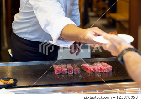Chef in a white uniform serves freshly grilled wagyu beef skewers to a customer at a Tokyo market 123878058