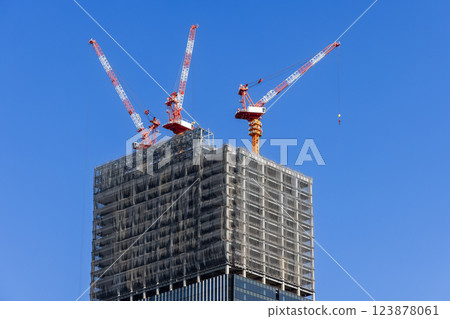 Three towering construction cranes operate atop a partially built skyscraper Three towering construction cranes operate atop a partially built skyscraper 123878061