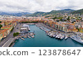 A stunning aerial view of Nice, France, showcasing its vibrant marina, luxurious yachts, colorful Mediterranean buildings, and lush green hills under a partly cloudy sky. 123878647