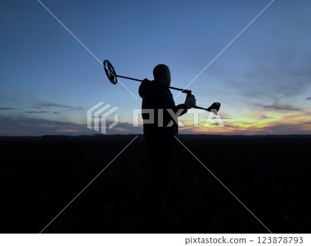 The silhouette of a treasure hunter at sunset. Treasure Hunter - Gold digger - Man Holding Metal Detector 123878793