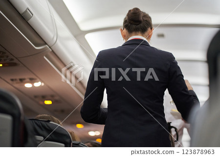 Rear view of a flight attendant in a black uniform on a plane with passengers. Hot drinks are served on board the aircraft. High quality photo Rear view of a flight attendant in a black uniform on a plane with passengers. Hot drinks are served on board the aircraft. High quality photo 123878963