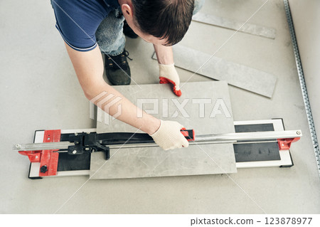 A machine for cutting large ceramic tiles into smaller tiles with precise dimensions. Close-up of the master cutting the tile into two parts with a machine. High quality photo A machine for cutting large ceramic tiles into smaller tiles with precise dimensions. Close-up of the master cutting the tile into two parts with a machine. High quality photo 123878977