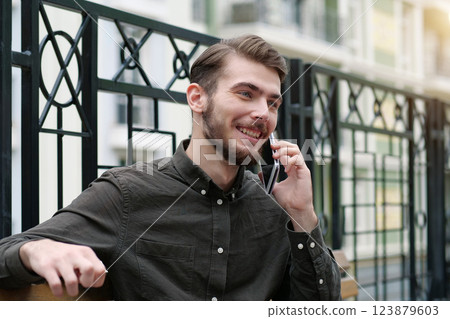 Handsome businessman sits on bench, speaks on cell phone and smiles 123879603
