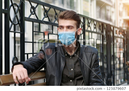 Sad depressed young man in medical protective face mask sits on the bench 123879607