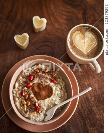 A delightful breakfast scene: creamy porridge with a cocoa heart, a latte with heart art, and heart-shaped chocolates on a wooden table 123879898