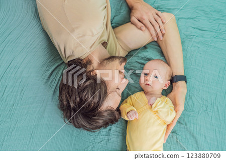 A father and his newborn baby lie on a soft muslin swaddle head to head, sharing a tender moment of closeness and bonding that highlights new beginnings and gentle parenting 123880709