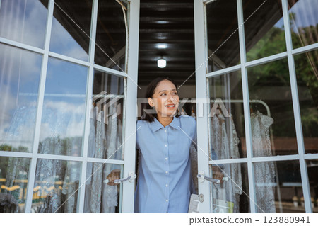 A smiling woman stands at her cozy houses open door, inviting warmth and joy A smiling woman stands at her cozy houses open door, inviting warmth and joy 123880941