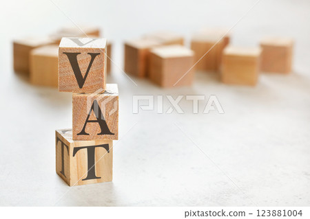 Three wooden cubes with letters VAT (means Value Added Tax), on white table, more in background, space for text in right down corner 123881004