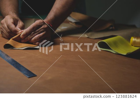 Shoemaker stitching leather pieces on wooden table in workshop 123881624