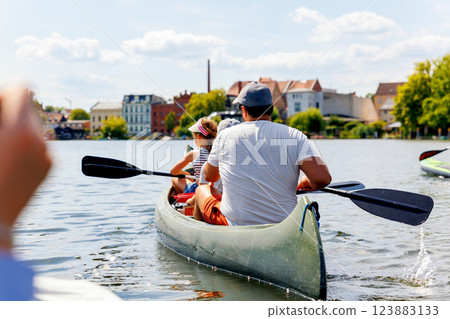 Man with two children enjoy having fun paddling canoe rent across lake river water wearing bright orange life vests hot sunny summer day. Healthy recreational activity lifestyle vacation trip journey Man with two children enjoy having fun paddling canoe rent across lake river water wearing bright orange life vests hot sunny summer day. Healthy recreational activity lifestyle vacation trip journey 123883133