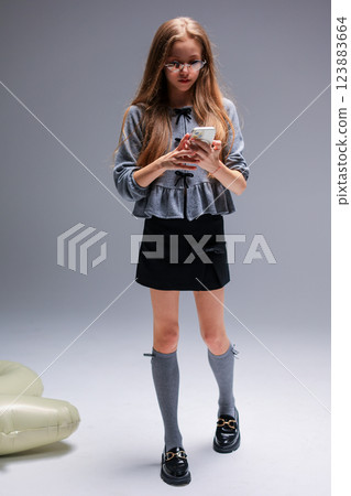 A Trendy Young Girl with Phone, Impressively Showcasing Modern Fashion Styles and Trends 123883664