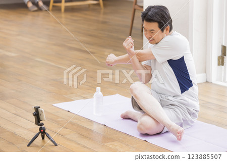 Elderly man exercising while looking at his smartphone Elderly man exercising while looking at his smartphone 123885507
