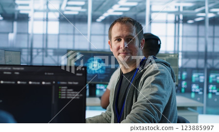 Portrait of joyous IT expert in server farm ensuring valuable data remains shielded from threats. Upbeat technician safeguarding data center hardware, securing system, camera A Portrait of joyous IT expert in server farm ensuring valuable data remains shielded from threats. Upbeat technician safeguarding data center hardware, securing system, camera A 123885997