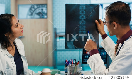 Indian healthcare expert sharing medical expertise with a patient in office, reviewing x ray scans and MRI diagnostics to focus on accurate treatment and recovery. Insurance consultation. Camera A. 123885999
