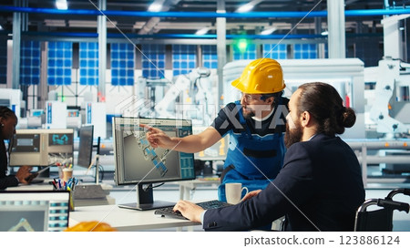 Photovoltaics factory manager with disability in wheelchair gives worker. Solar panels plant supervisor with paraplegia in inclusive workspace talking with employee, camera A Photovoltaics factory manager with disability in wheelchair gives worker. Solar panels plant supervisor with paraplegia in inclusive workspace talking with employee, camera A 123886124