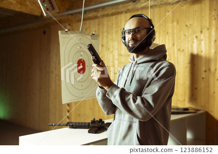 Portrait of smiling Arab man in shooting range trying out new gun model before committing to purchase. Middle Eastern person in indoor firing range learning how to operate new weapon safely 123886152