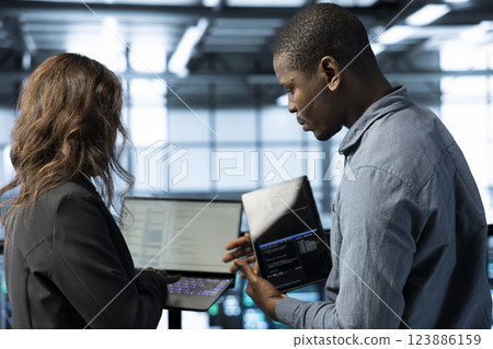 System administrators in data center using laptop and tablet, integrating green technologies. IT specialists in server room using devices to implement sustainable energy solutions 123886159