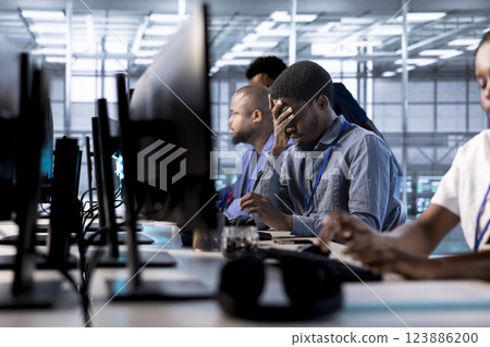 Tired engineer feeling headache while reconfiguring server farm to optimize it for data processing requirements. Stressed man working overtime to ensure data center gear operates efficiently 123886200