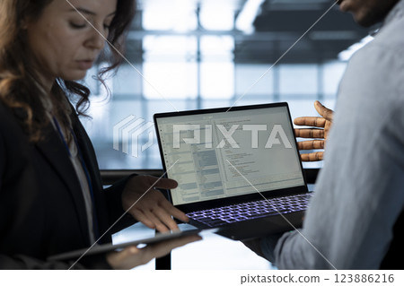 Software developers in data center workspace use laptop to calibrate energy usage. Server room IT professionals code on notebook, doing maintenance on equipment mainframes Software developers in data center workspace use laptop to calibrate energy usage. Server room IT professionals code on notebook, doing maintenance on equipment mainframes 123886216