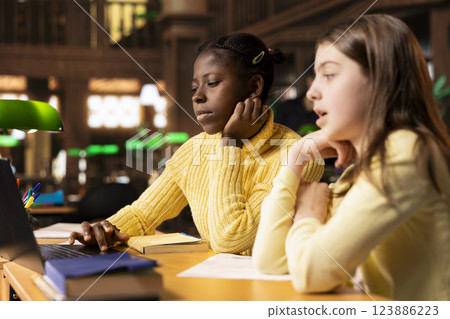 Diverse preteen students in the library engaged in e learning seminar, participating in a video conference for a school assignment. Young girls attend online webinar with tutor, social meeting. Diverse preteen students in the library engaged in e learning seminar, participating in a video conference for a school assignment. Young girls attend online webinar with tutor, social meeting. 123886223