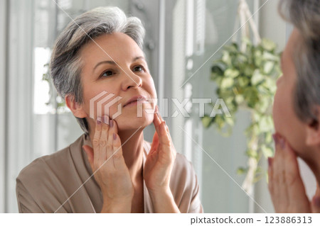 Smiling elderly woman of the age of a pensioner iwith gray hair does herself a manual facial massage 123886313