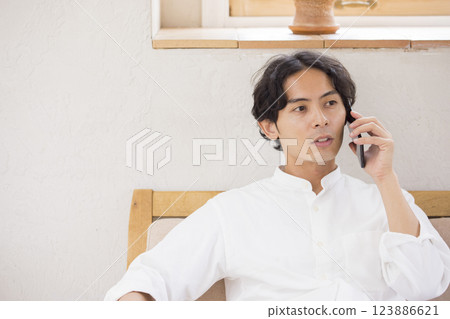 A young man sitting on a sofa and talking on a smartphone 123886621