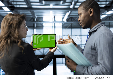 Admins in data center using mockup tablet, observing analytics, reviewing infrastructure health. Server hub IT coworkers discussing, using chroma key device, adjusting system parameters 123886962