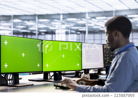 Employee using isolated screen PC to check for signs of failure in data center supercomputers. Engineer working at multi monitor chroma key PC to prevent damages in server farm, monitoring systems 123887005