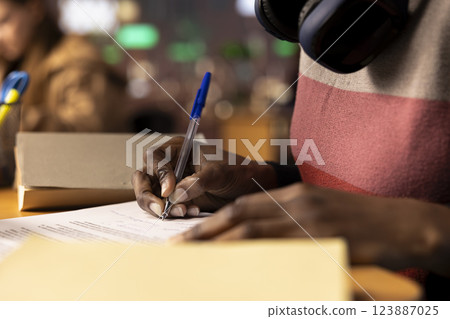 Black university scholar completing a detailed course project using educational resources and materials from the college library general database. Girl working hard on her academic notes. Close up. Black university scholar completing a detailed course project using educational resources and materials from the college library general database. Girl working hard on her academic notes. Close up. 123887025