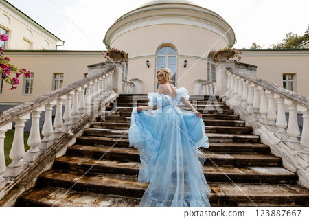 Elegant Woman in a Flowing Blue Gown Walking Down the old stone Stairs. Back view. 123887667