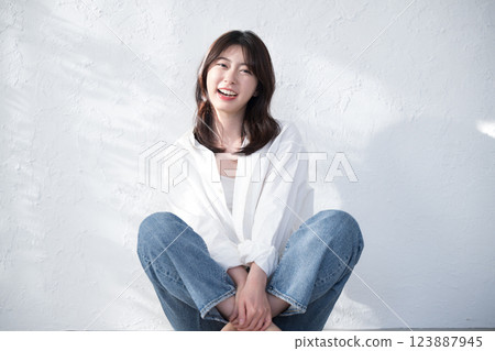 Full body of a smiling woman sitting on a white background with sunlight Stylish denim fashion 123887945