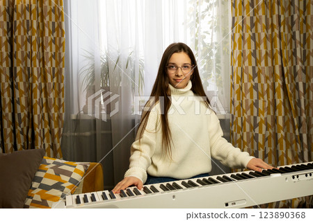 Girl in glasses sitting at piano, looking at camera Girl in glasses sitting at piano, looking at camera 123890368