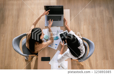 Two women are sitting at a table with laptops and papers in front of them Two women are sitting at a table with laptops and papers in front of them 123891085