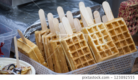 Several delicious Belgian waffles on a stick are displayed and ready to be served at a food market. 123892555