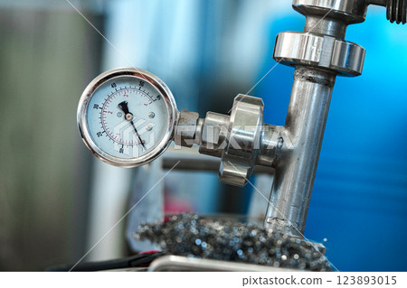 A pressure gauge is attached to a metal pipe in a factory setting 123893015