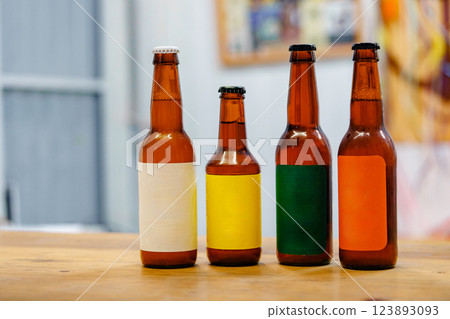 Four bottles of beer with different colored labels sit on a wooden table 123893093