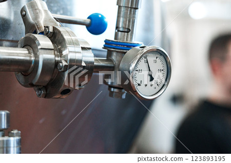 A close-up of a pressure gauge attached to a stainless steel pipe in a factory 123893195