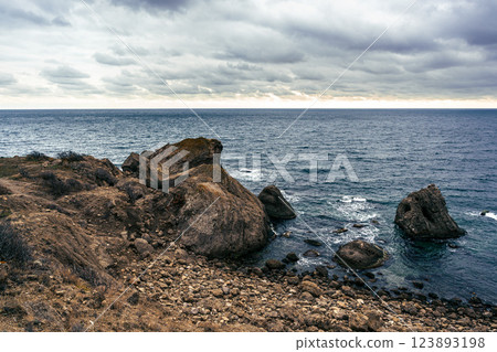 Rocky coastline under a dramatic sky with turbulent sea waves in the late afternoon 123893198