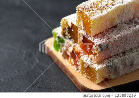 Colorful traditional sweets stacked on a wooden board with coconut flakes 123893239
