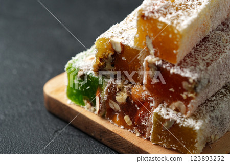 Colorful Turkish delight stacked on a wooden board with a textured background and a sprinkle of coconut 123893252