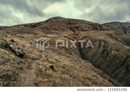 Hikers travel across a rugged mountain landscape under a cloudy sky in a remote area during early morning hours 123893298