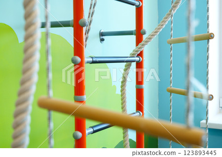 Indoor play area features colorful climbing frame with ropes and wooden bars for children's physical activity and fun 123893445