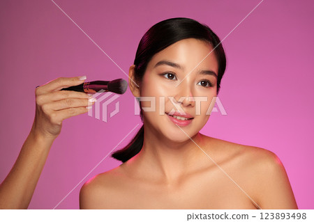 Makeup application on a model with a pink background during a beauty shoot 123893498